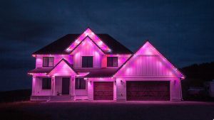 A large house is illuminated with vibrant pink lights against a dark sky