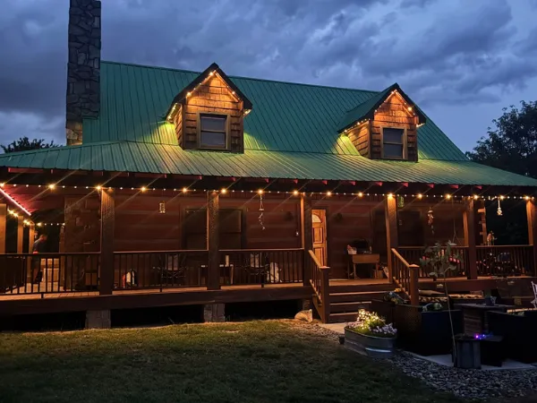 A rustic cabin glows warmly under evening skies, adorned with festive lights