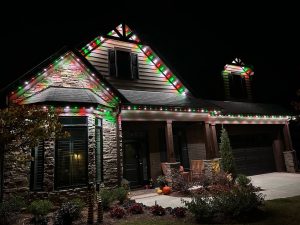 A cozy home is illuminated with festive red and green lights against a dark sky