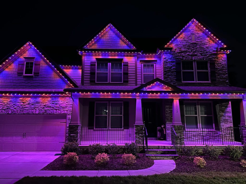 A house is adorned with vibrant purple and blue lights against a dark sky