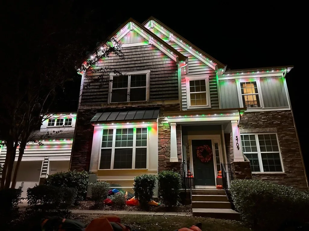 A house is adorned with colorful Christmas lights, glowing against the night sky