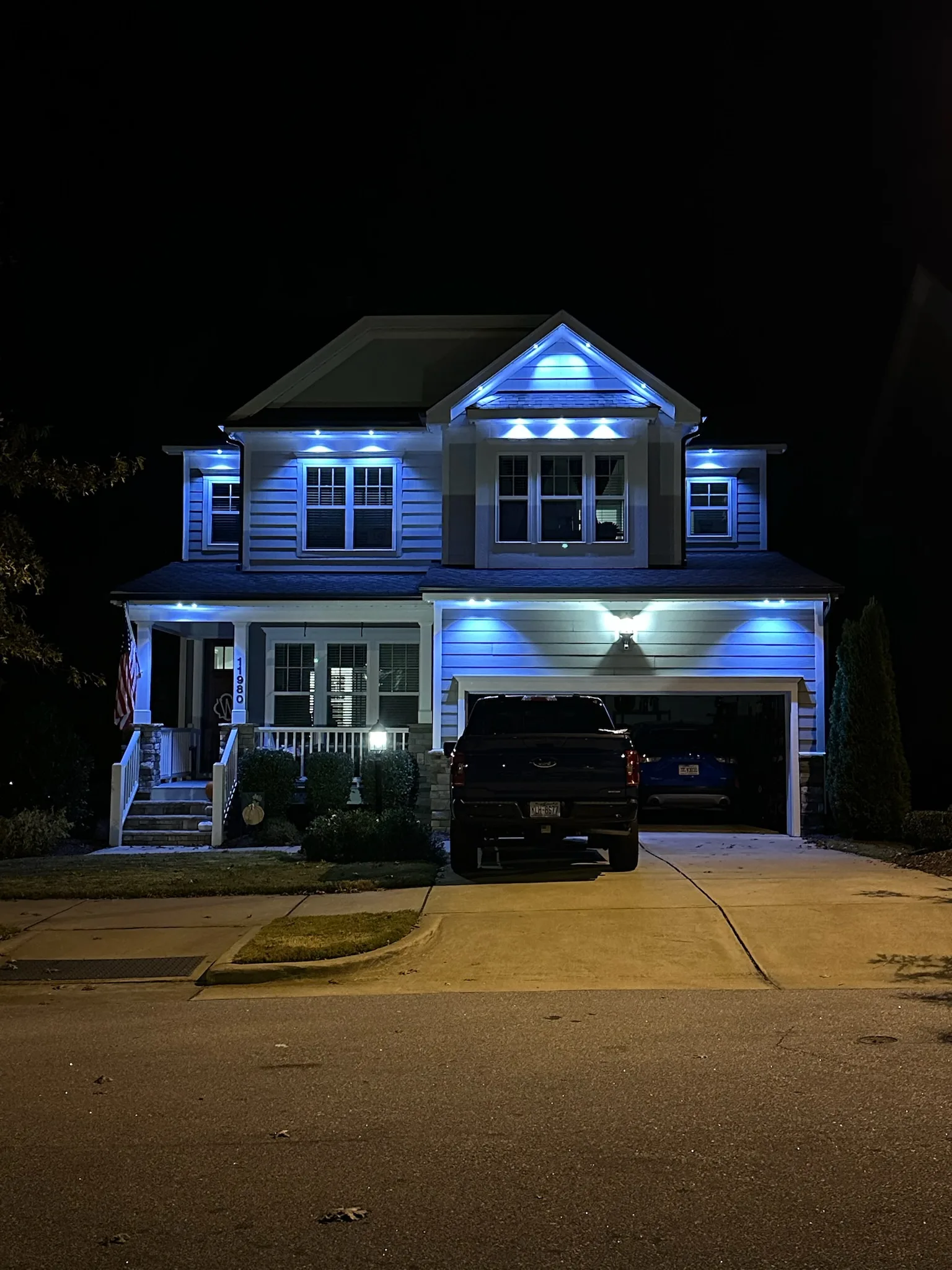A well-lit house with blue lights shining against a dark night sky