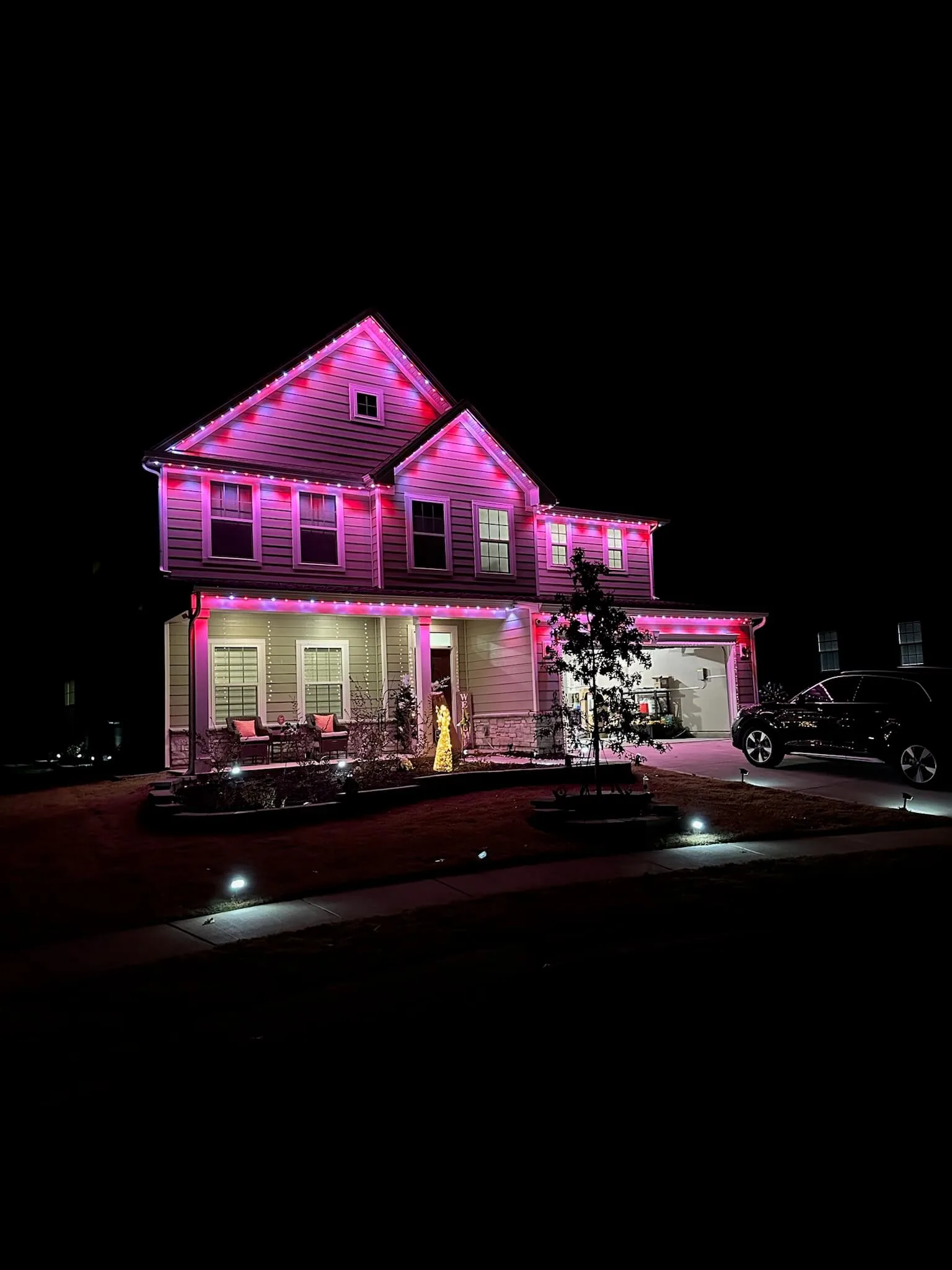 Permanent Christmas lights illuminate a house with vibrant pink hues in the night