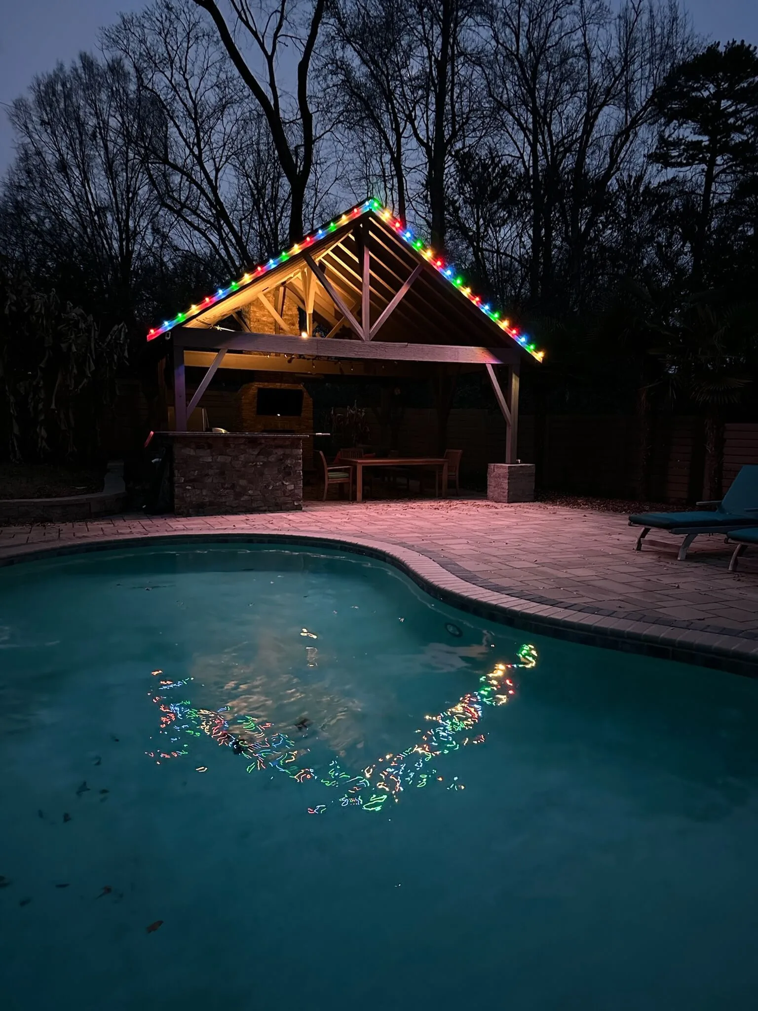 A brightly lit gazebo reflects colorfully in the dark swimming pool