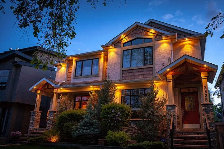 A beautifully illuminated house stands amidst lush greenery in the twilight