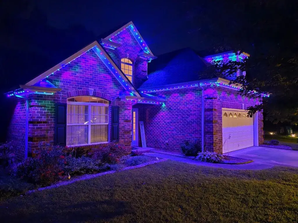 A beautifully illuminated brick house is adorned with vibrant blue and purple lights at night